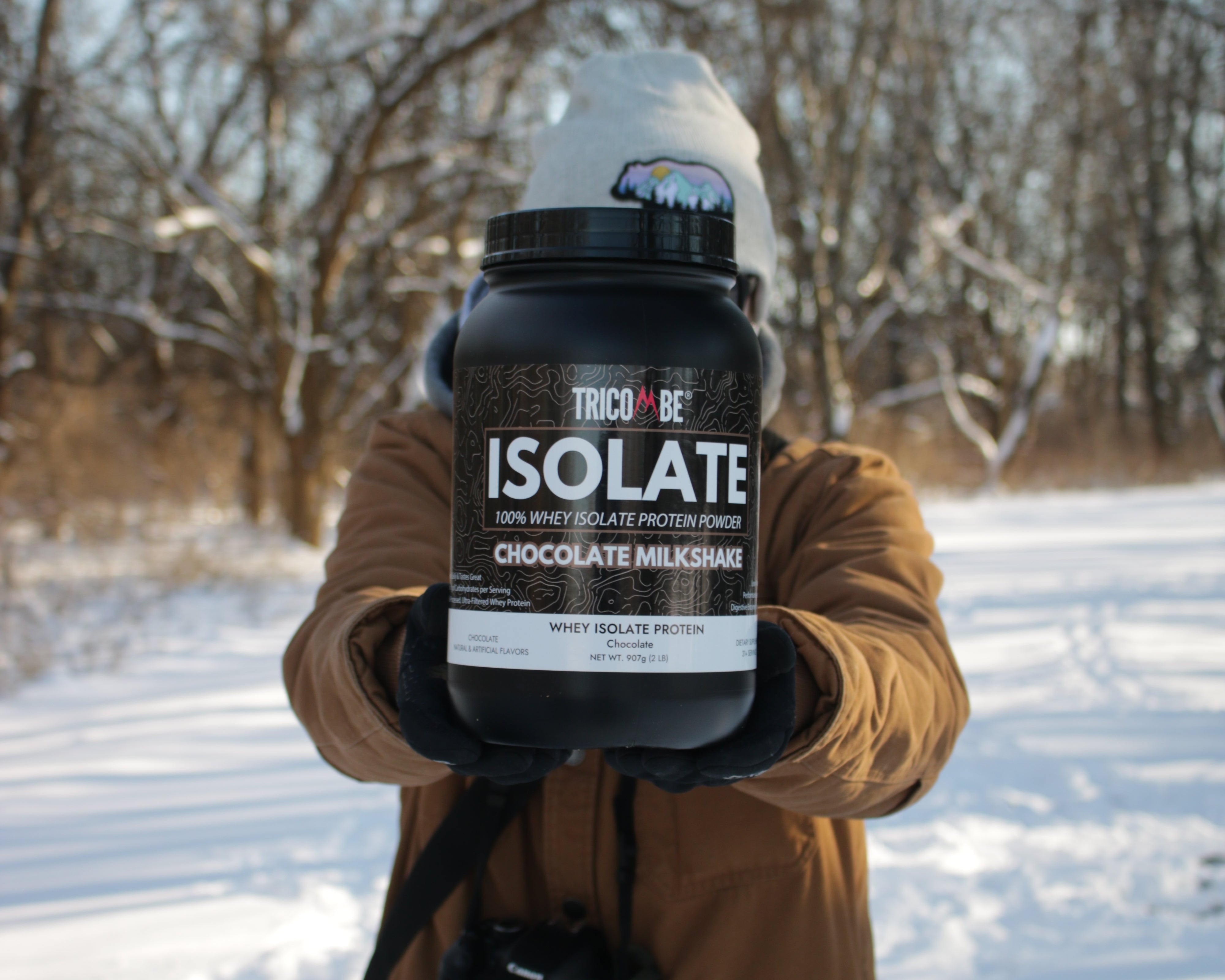 Person holding a protein supplement bottle in a snowy landscape